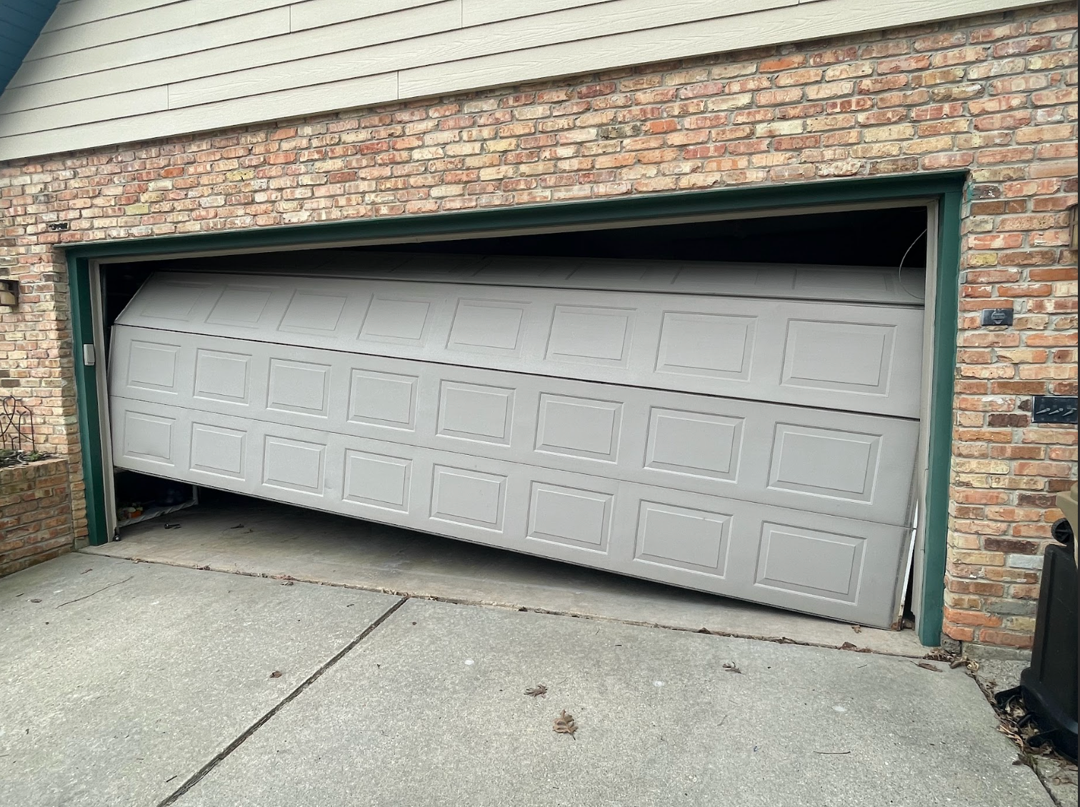 A broken garage door is sitting on the side of a brick building.