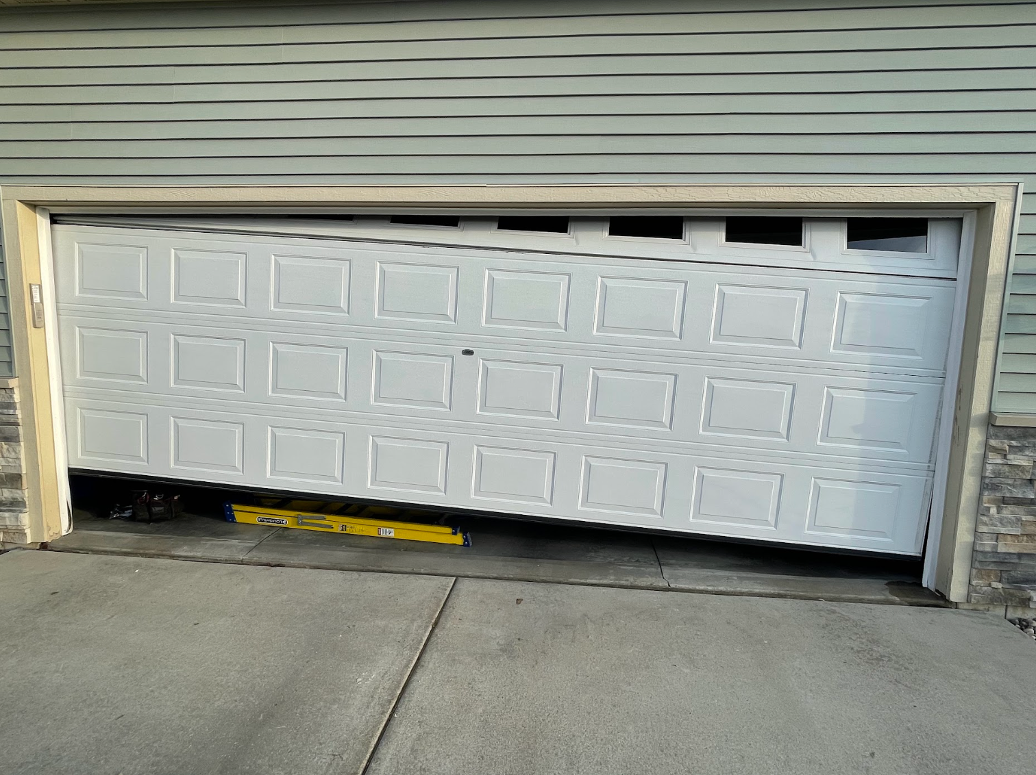 A white garage door that is open and broken