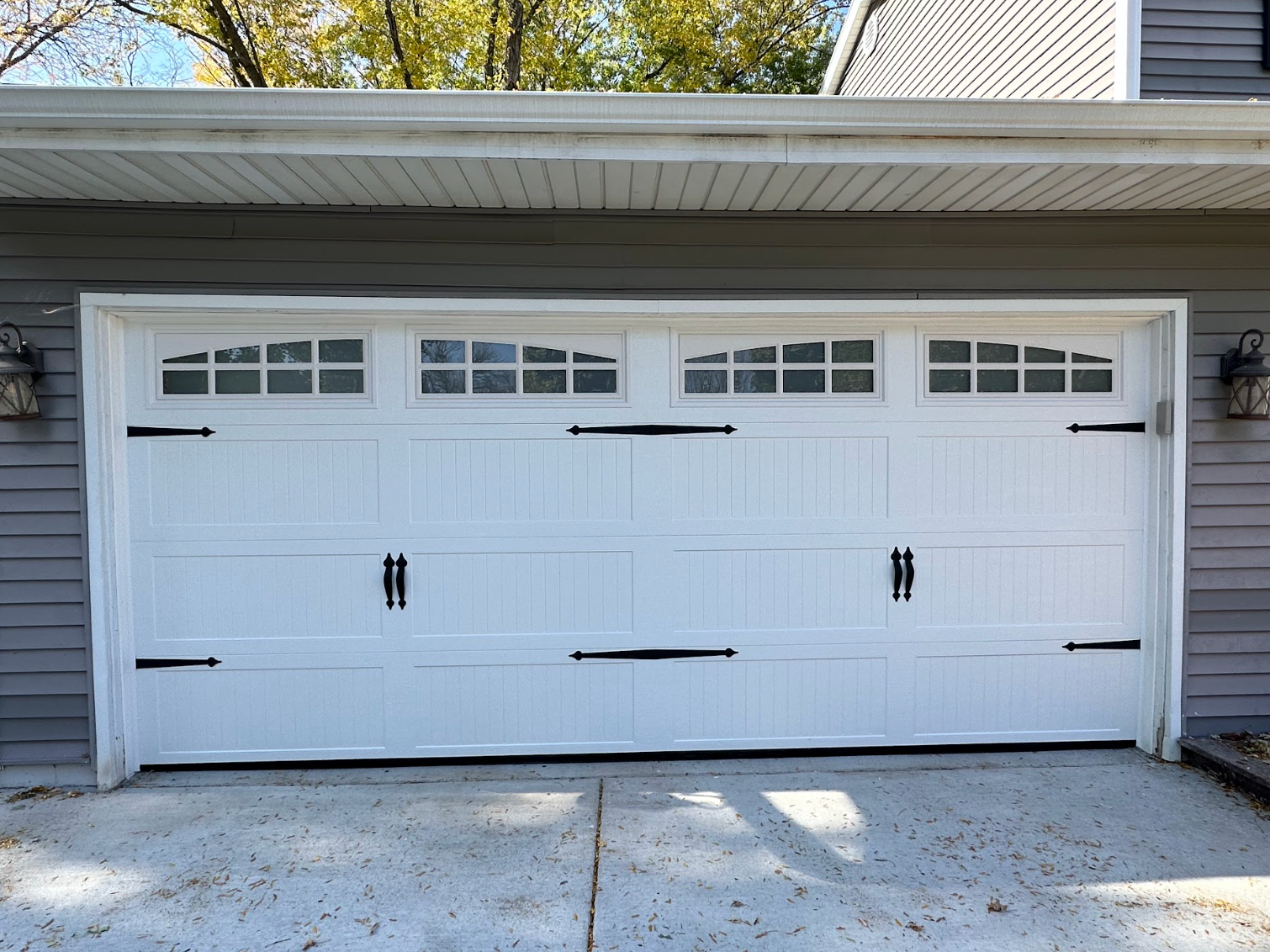 A white garage door is sitting in front of a gray house.