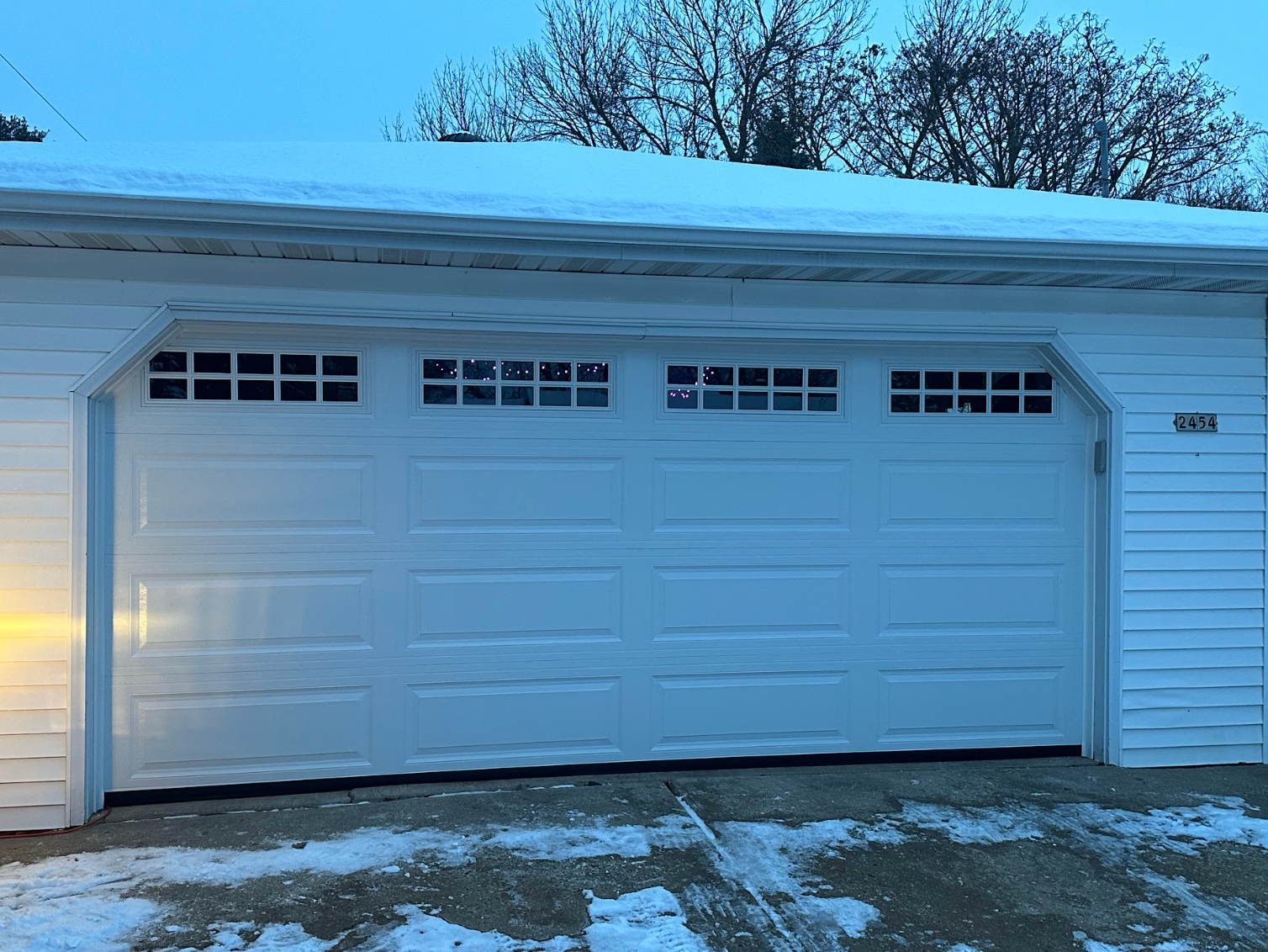 A white garage door is open in the snow.