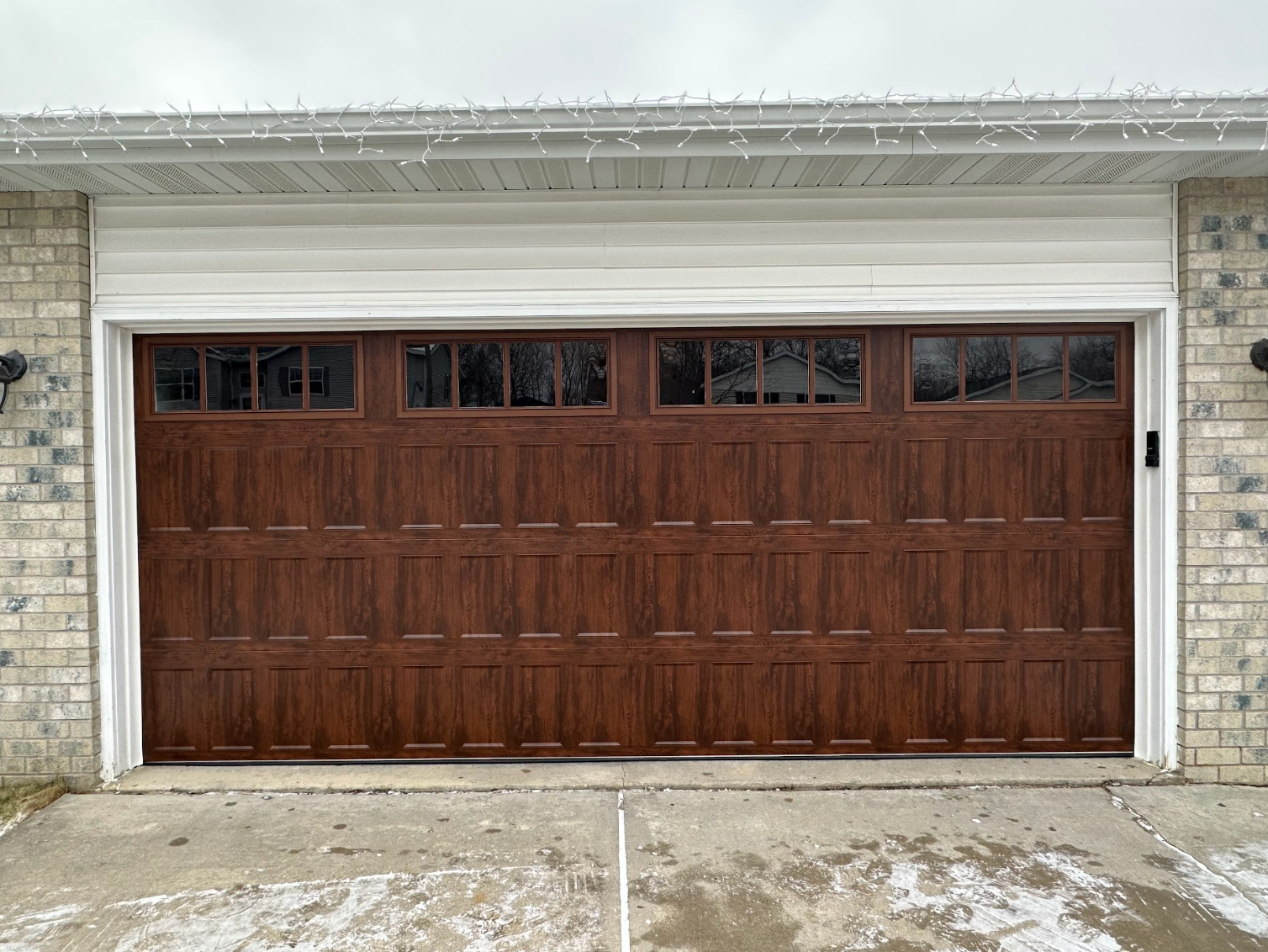 A large wooden garage door is sitting in front of a brick house.