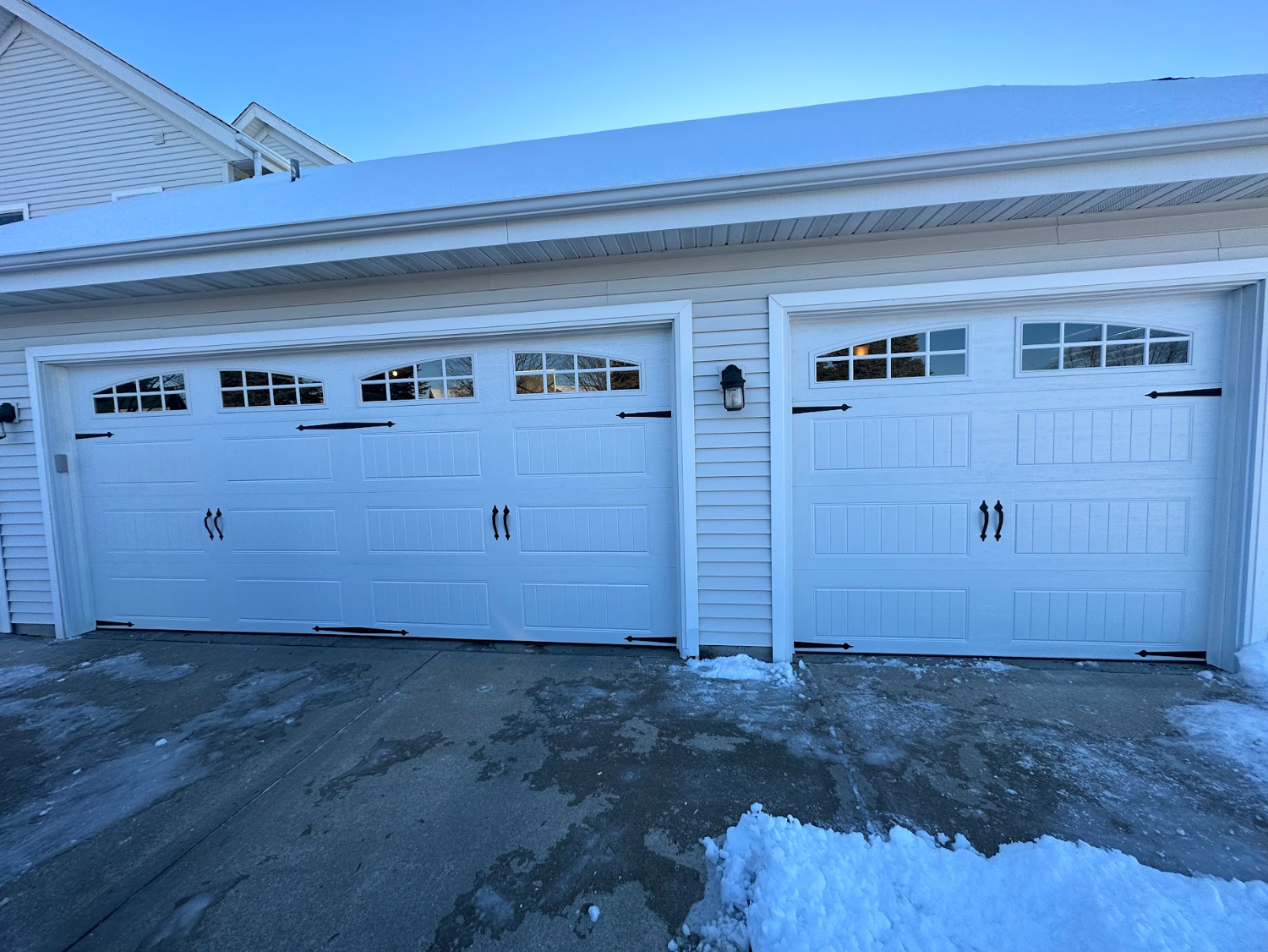 Three white garage doors on a house with snow on the ground
