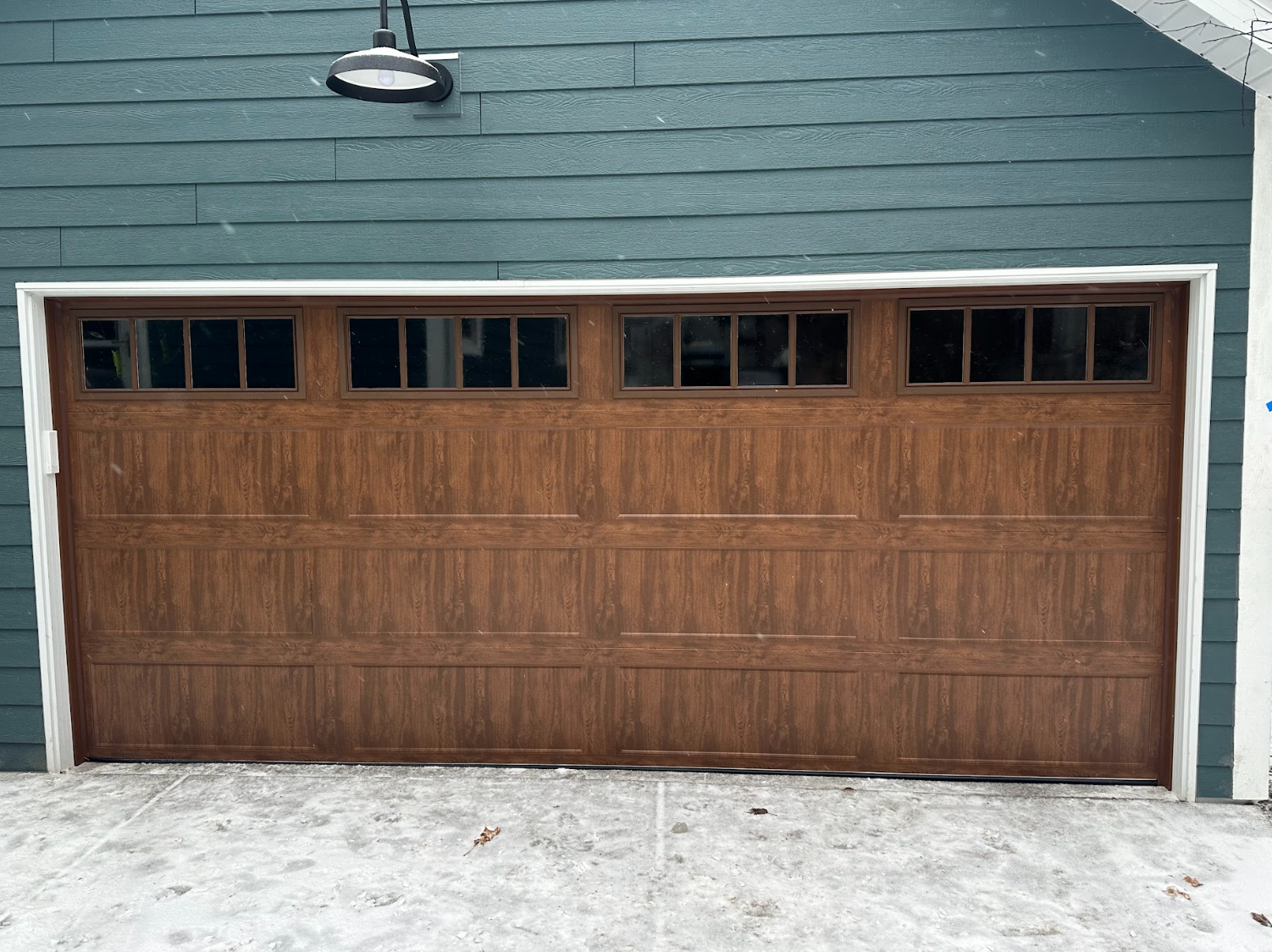 A brown garage door is sitting in front of a blue house.