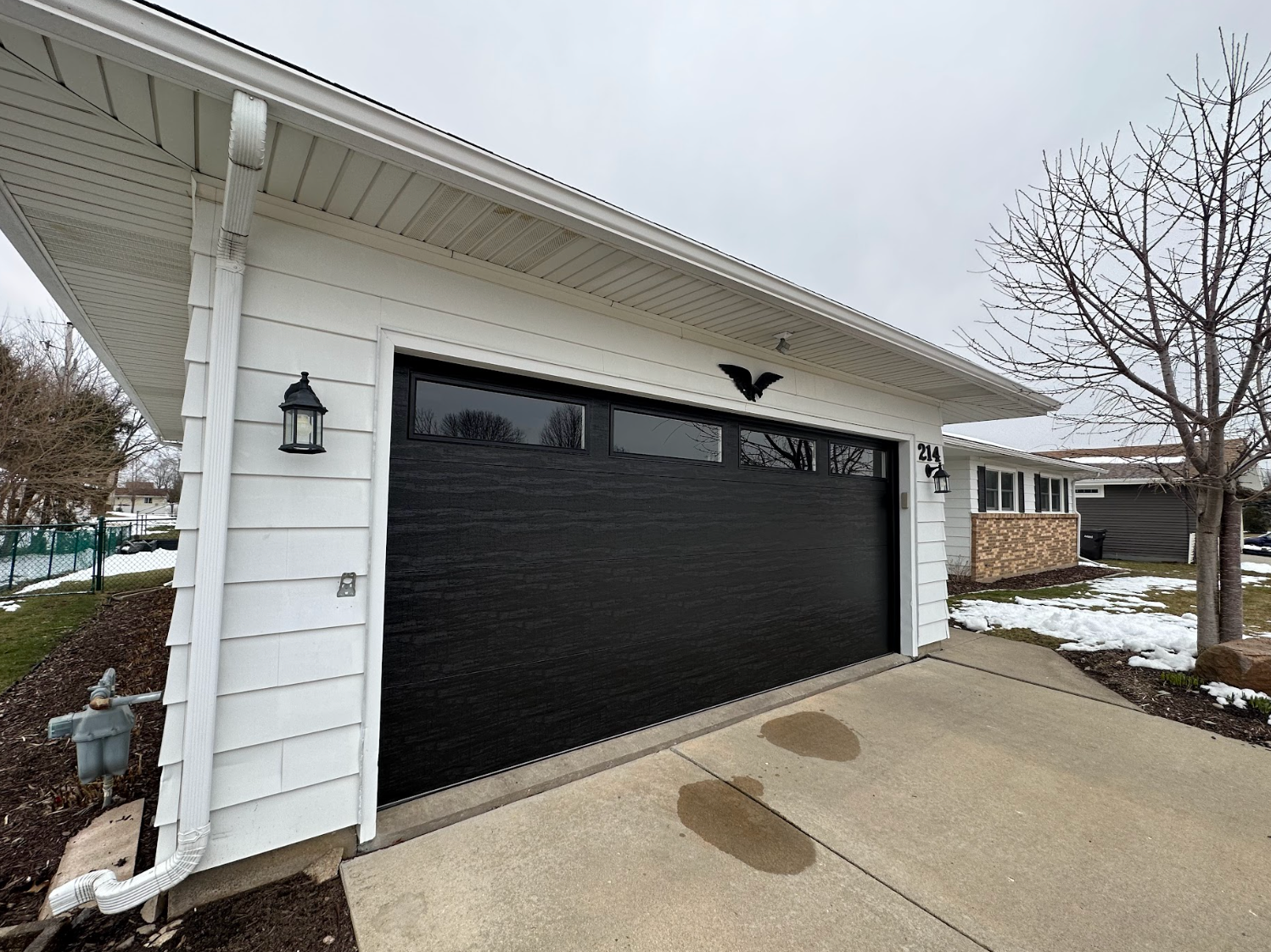 A black garage door is on the side of a white house.