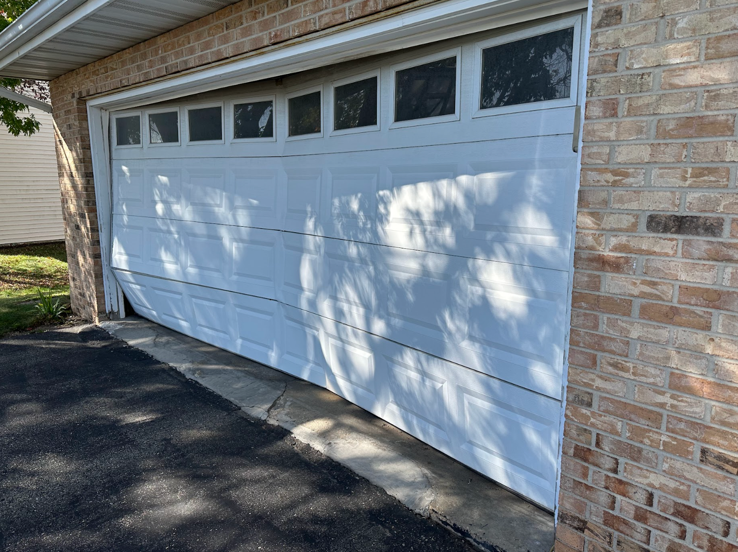 A white garage door is open on a brick house.