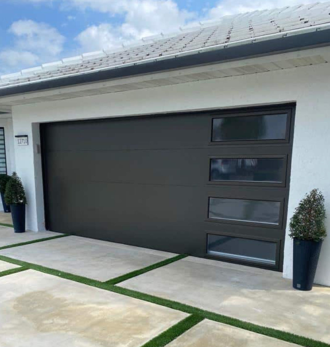 A black garage door is sitting in front of a white house.