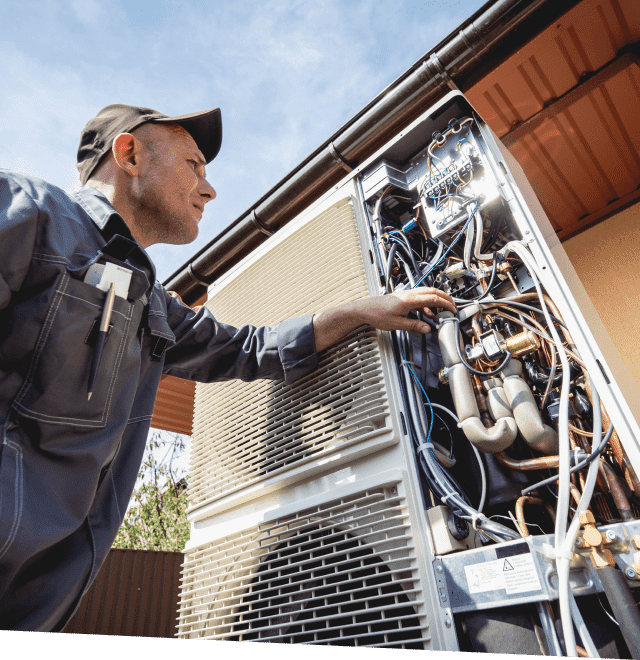 Mechanic examines an open HVAC unit outdoors, touching internal components.