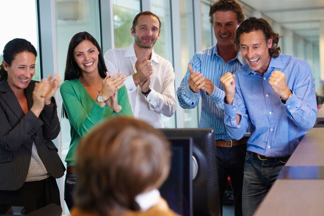 A group of people are applauding a woman in front of a computer screen.