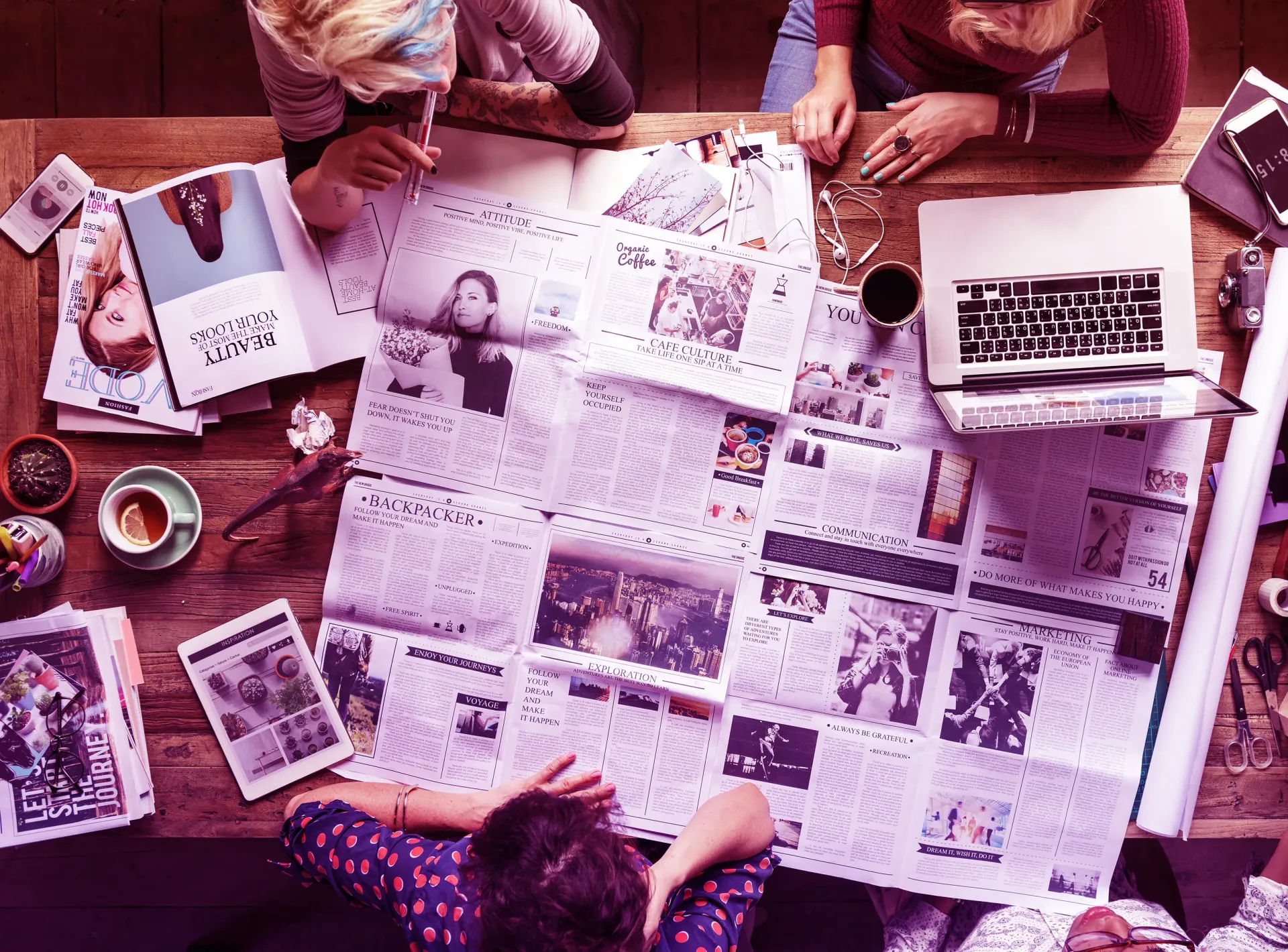 A group of people are sitting around a table looking at newspapers.