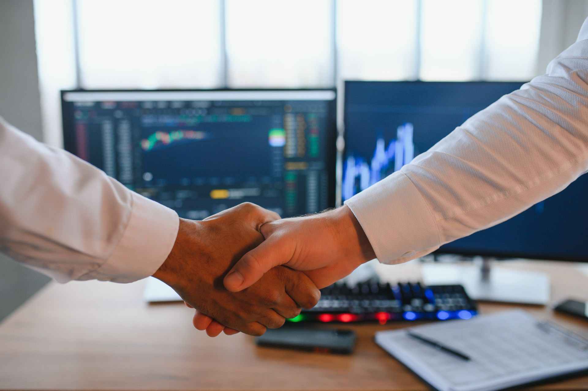 Two men are shaking hands in front of a computer screen.