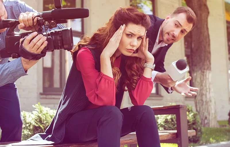 A woman is sitting on a bench while a man takes a picture of her.