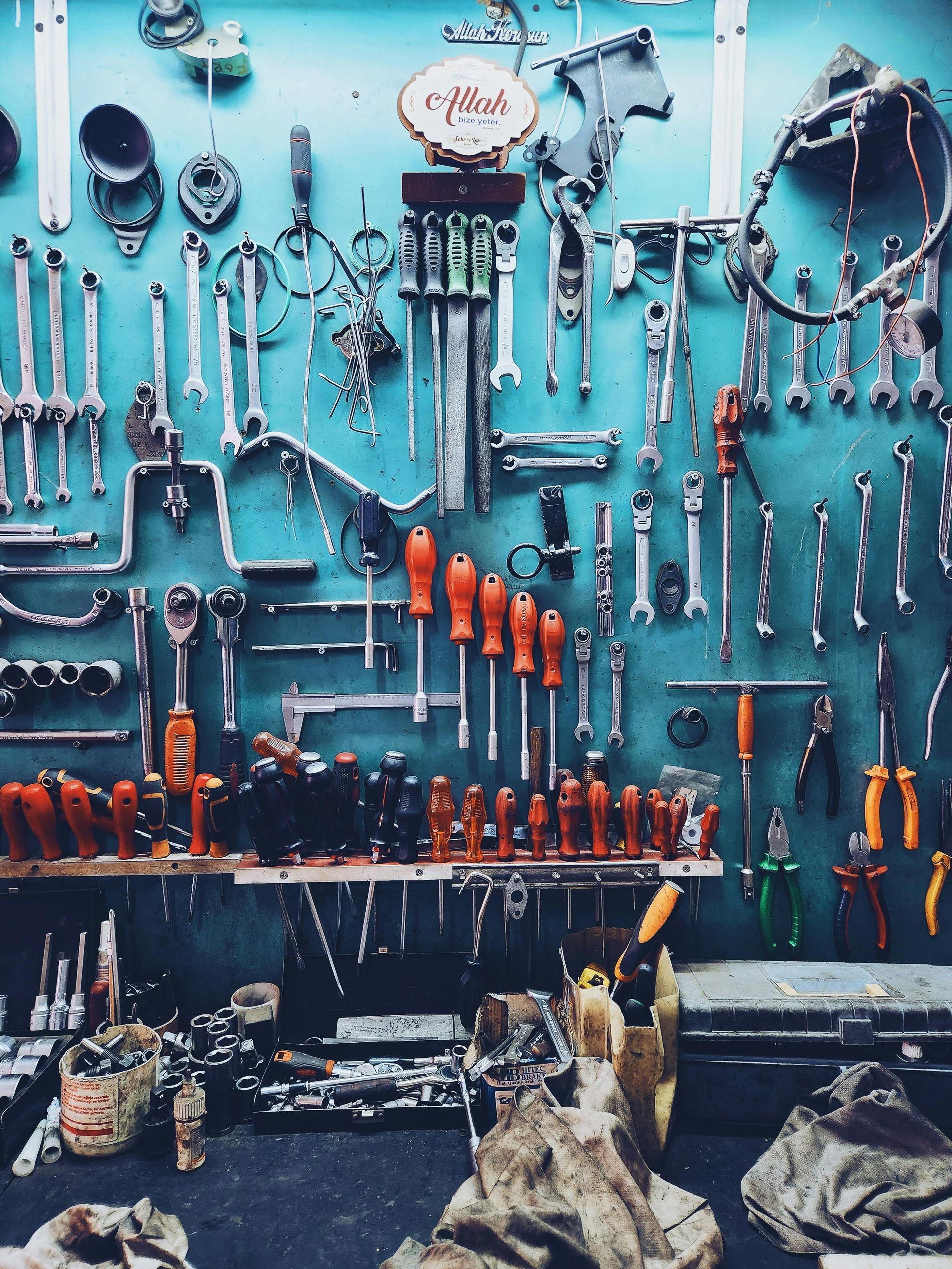 A turquoise wall covered in various tools like wrenches, screwdrivers, and pliers, organized on hooks and a shelf.