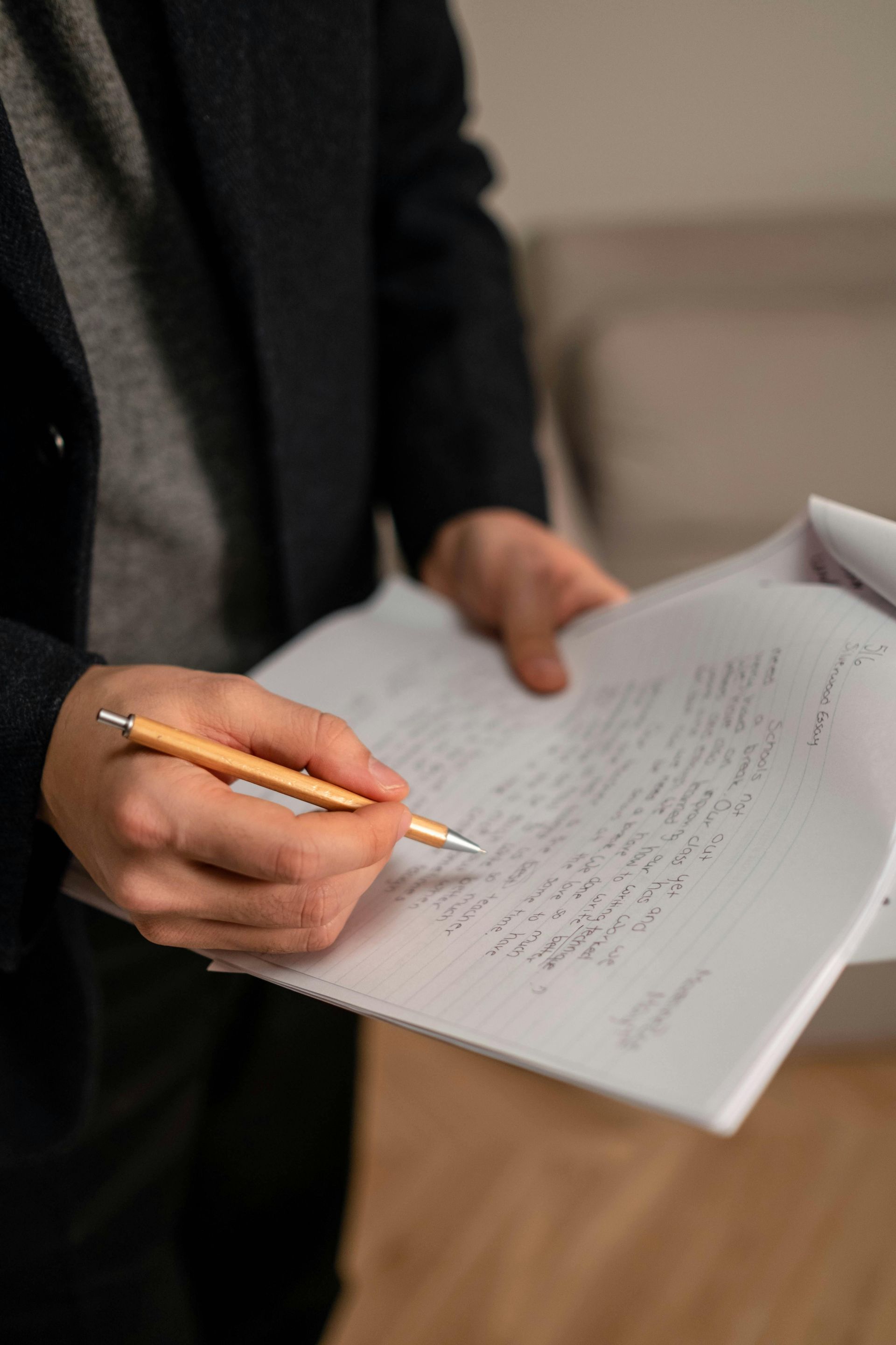 A person in a dark blazer holds a wooden pencil over a handwritten document on a notepad.