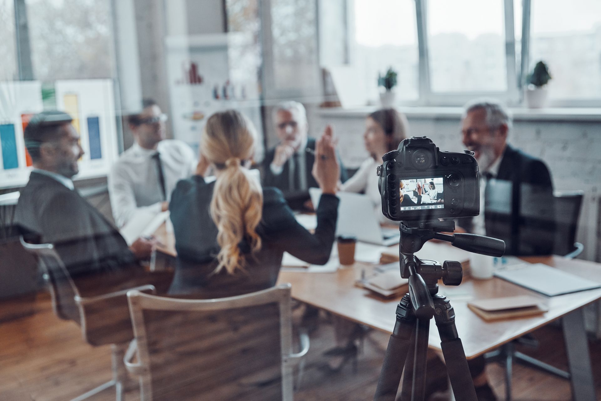 Camera on tripod filming a business meeting around a table.