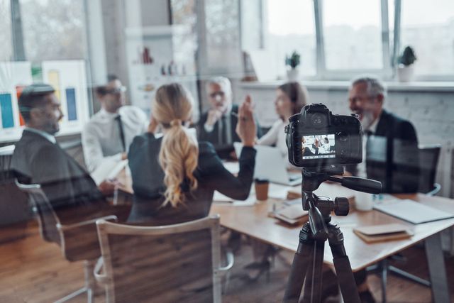 Camera on tripod filming a business meeting around a table.