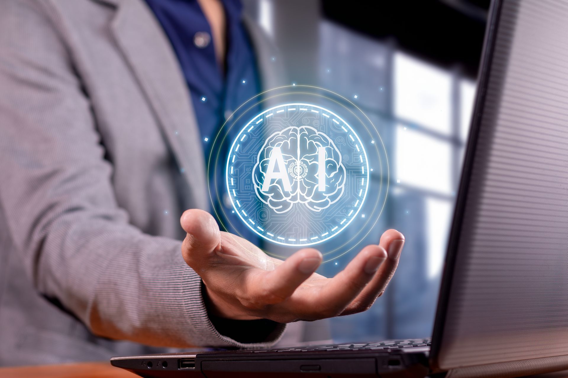 A man is holding a virtual brain in front of a laptop computer.