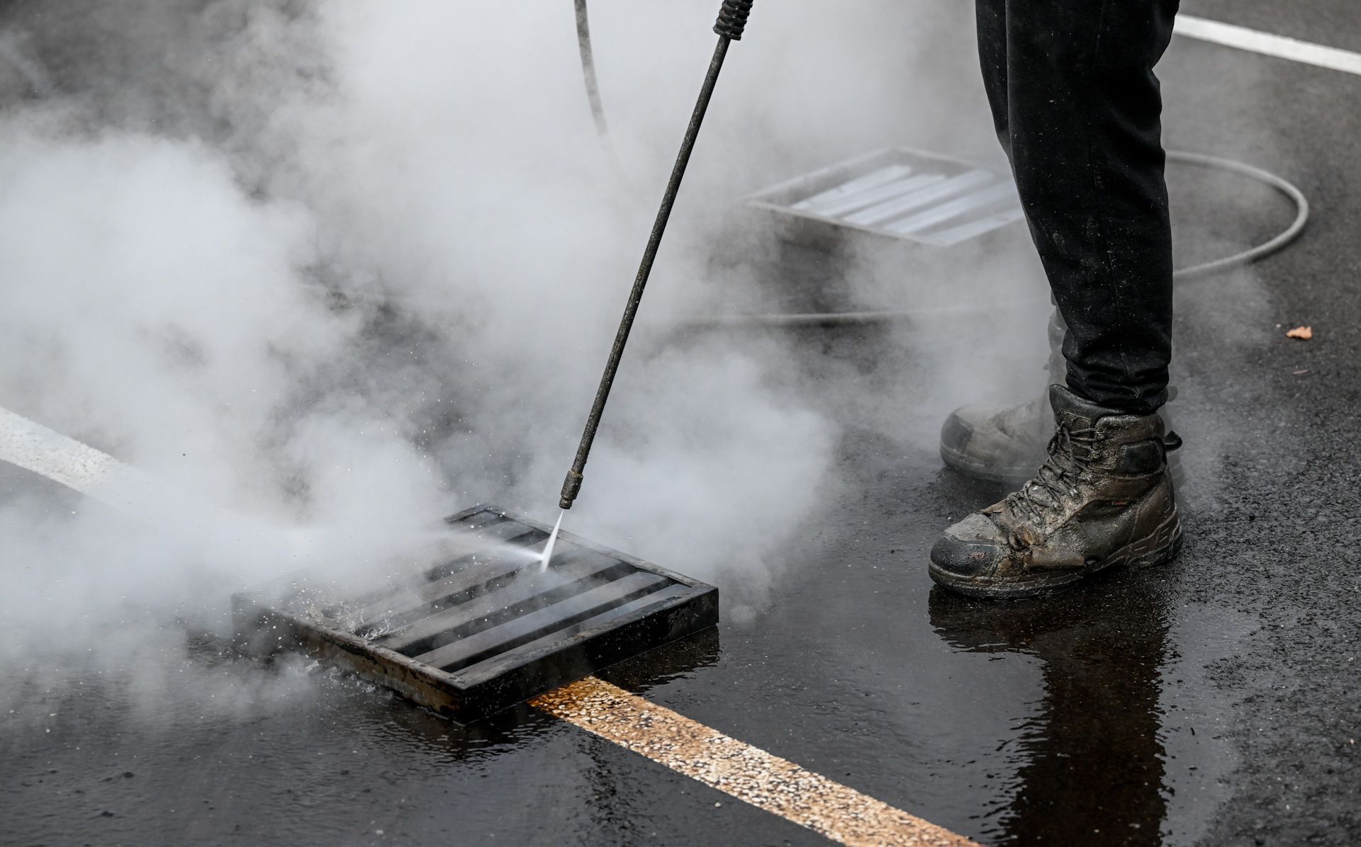 A person is cleaning a manhole cover with a high pressure washer.
