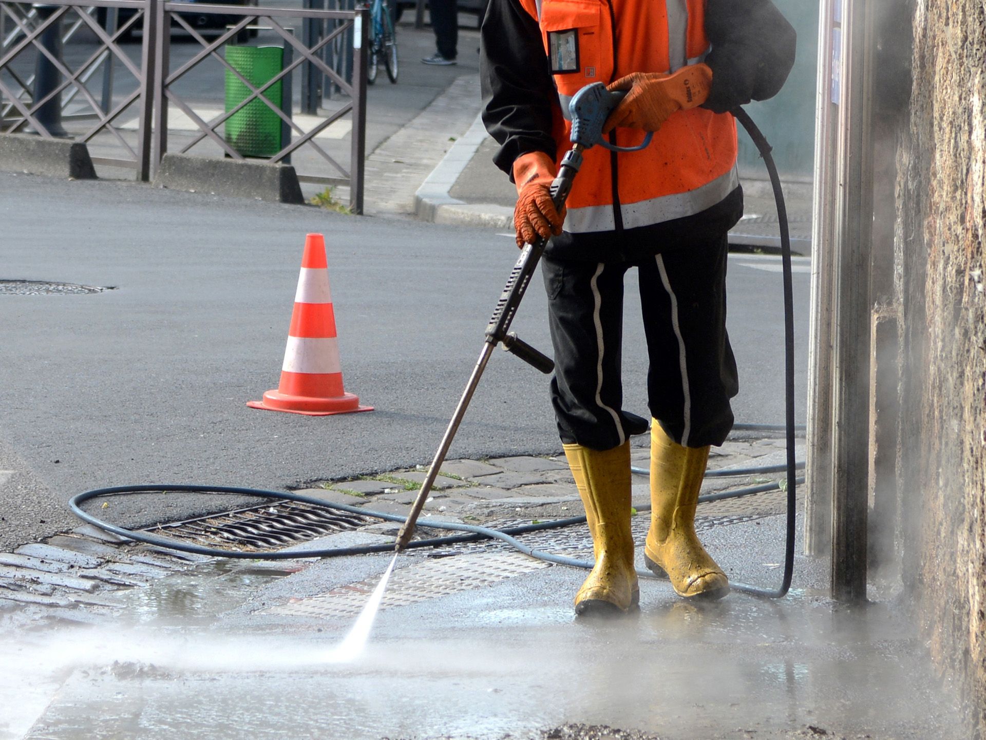 A man is using a high pressure washer to clean a manhole cover