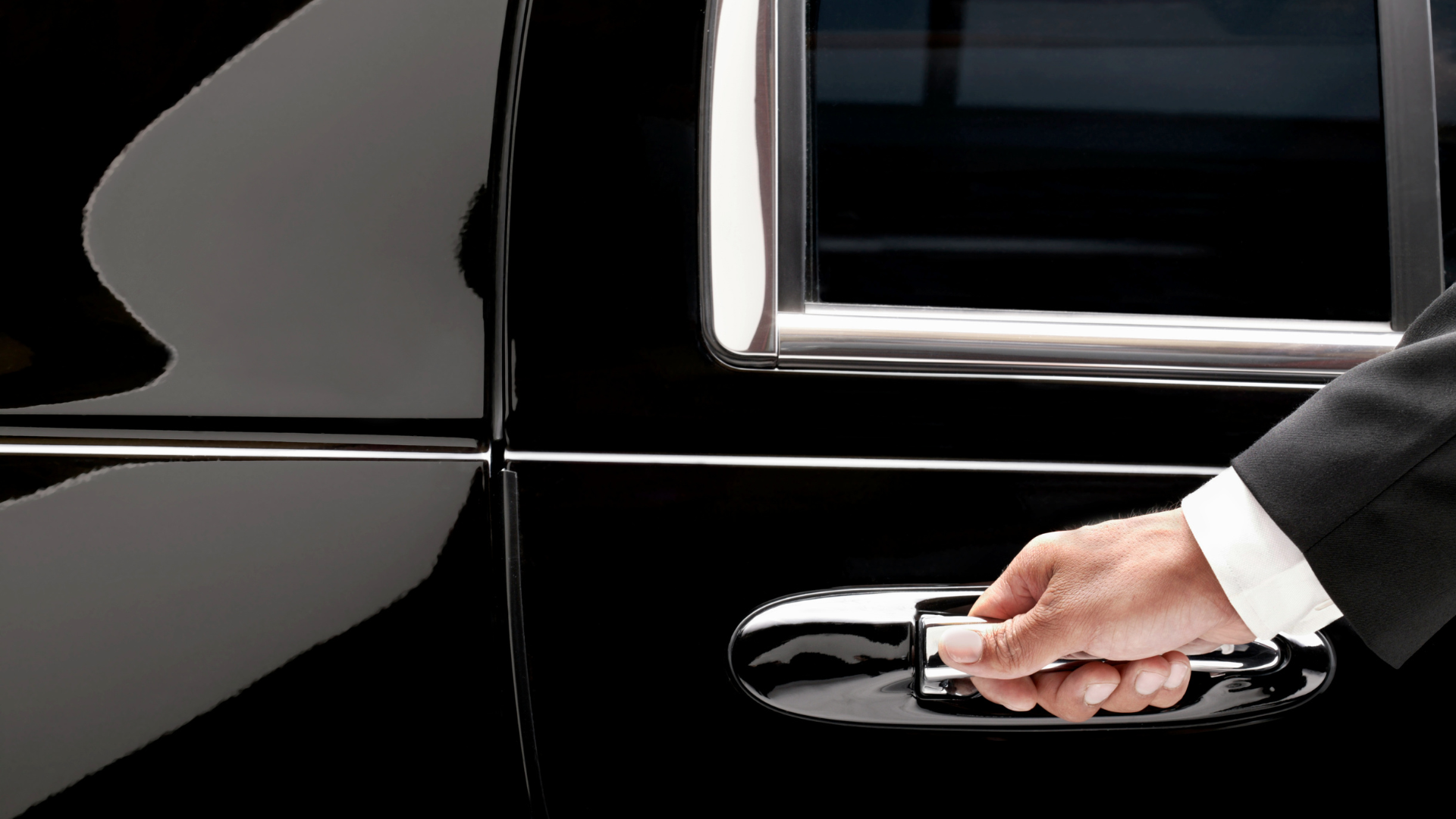 Hand opening the door of a black car. The person is wearing a suit.
