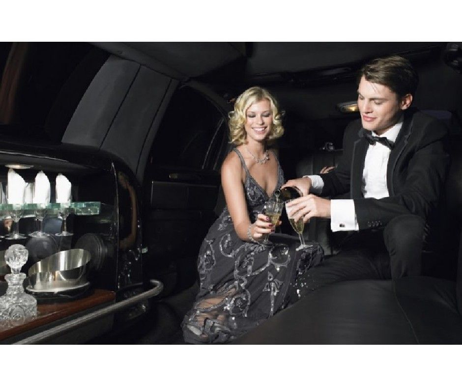 Man pouring champagne for a woman in a limousine. They are both dressed in formal attire.