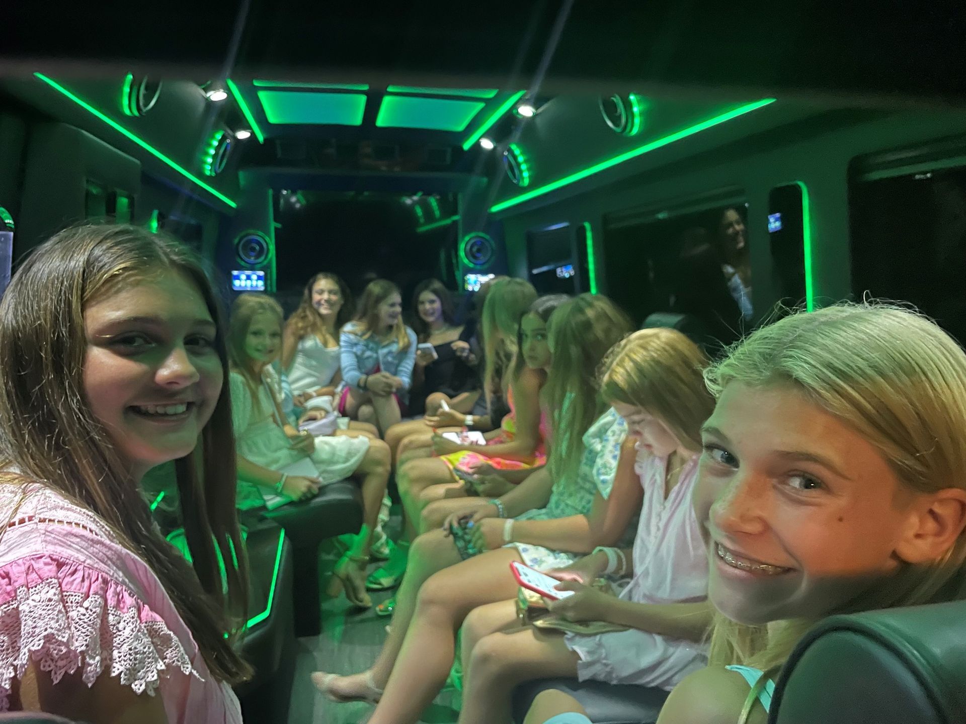 Girls smiling inside a party bus with green lights.