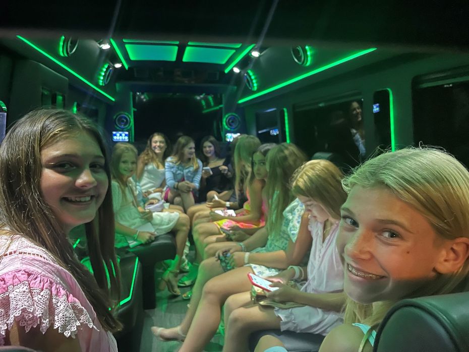 Girls inside a party bus with neon green lights. One girl smiles at the camera.