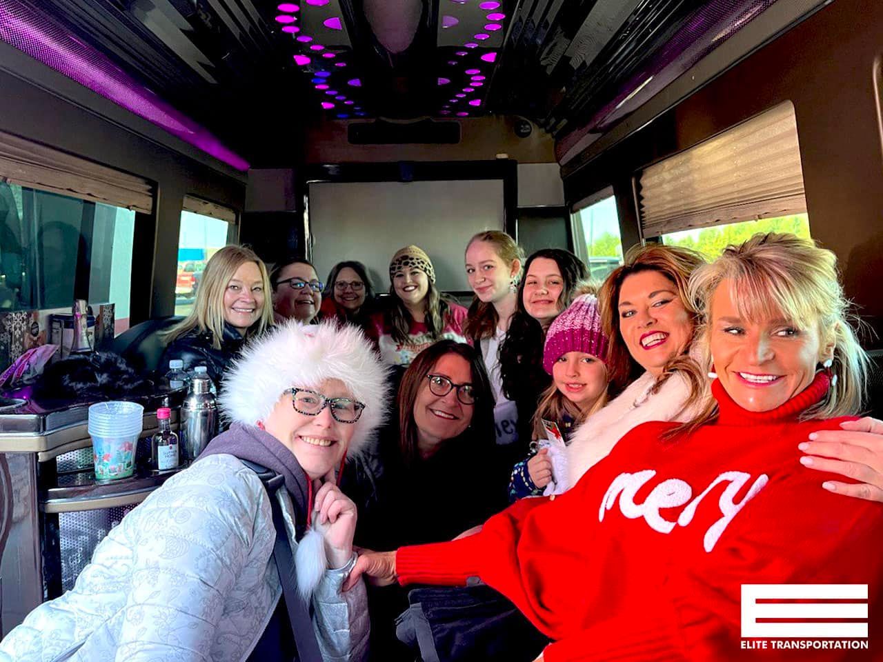 Group of women smiling inside a decorated van with purple lighting. One wears a red
