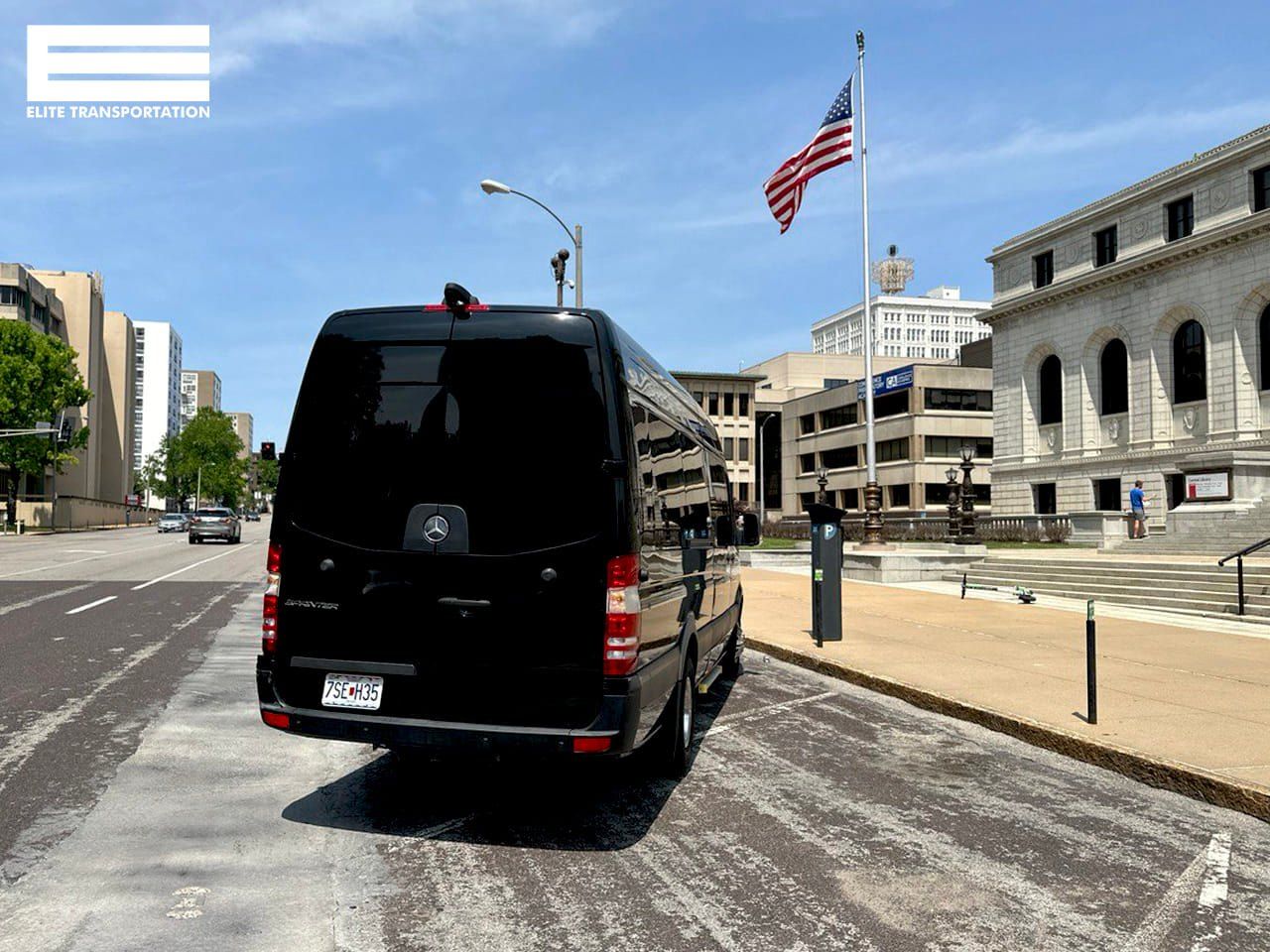 Black van parked on street with US flag and buildings in the background.