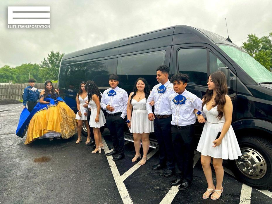 Group of people in formal attire pose near a black van; Quinceañera in blue/gold gown.