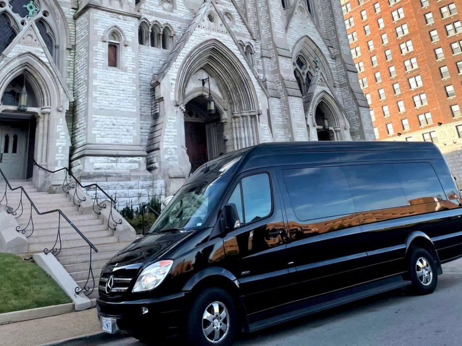 Black passenger van parked in front of a stone church with arched doorways.