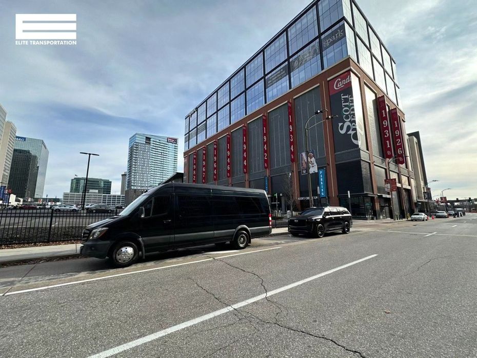 Black van and SUV parked on a city street, large building in the background.