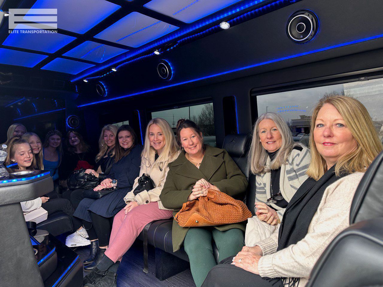 Group of people seated inside a black limousine with blue interior lights.