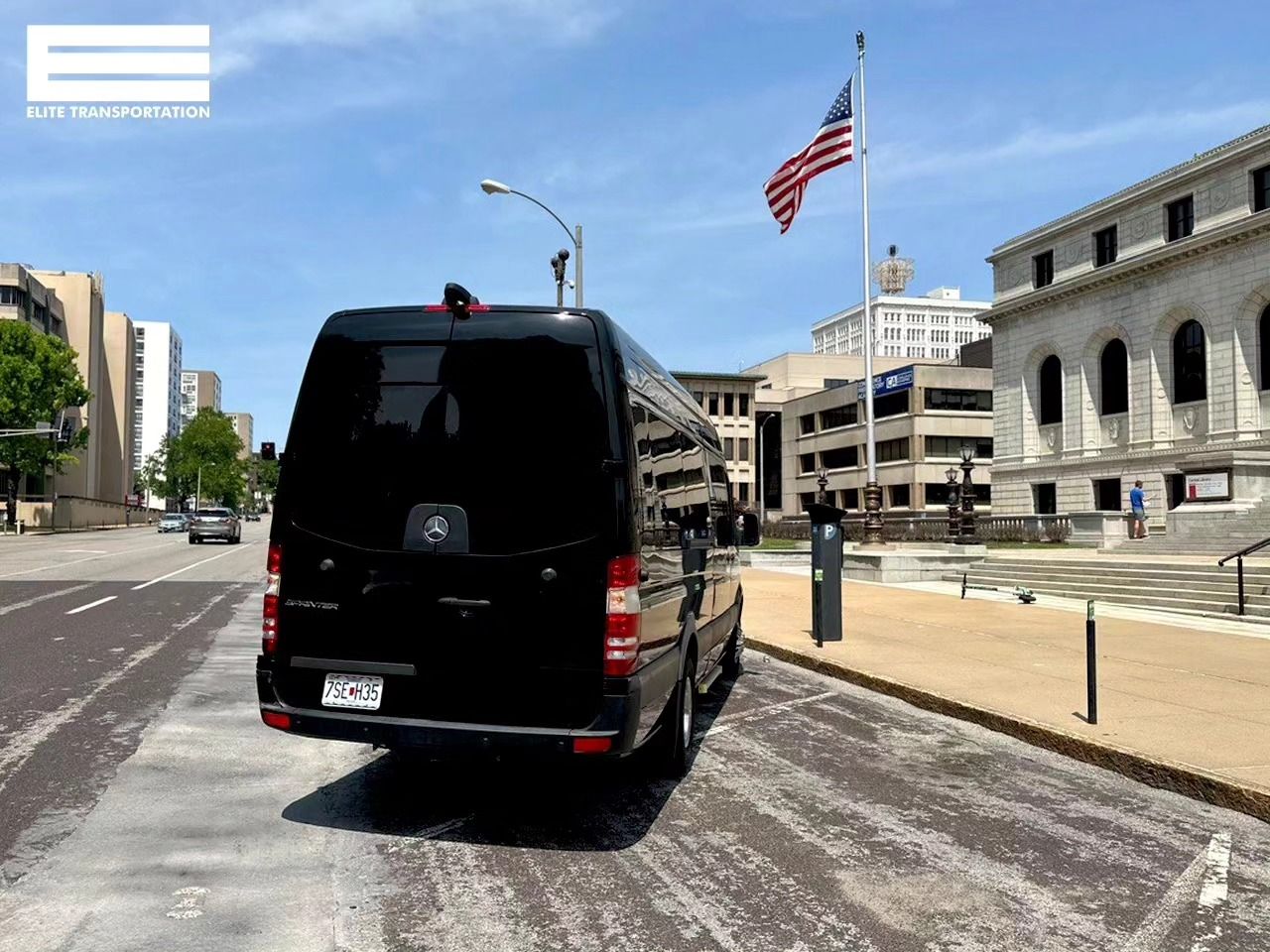 Black van parked by a building with an American flag on a sunny day.