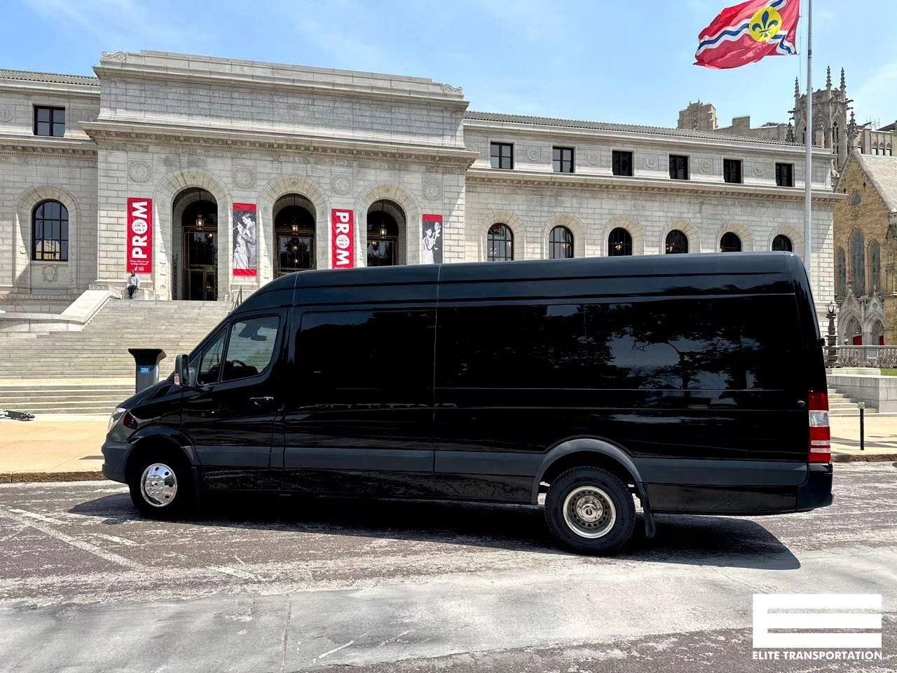 Black van parked in front of a stone building with stairs and a red and white flag.