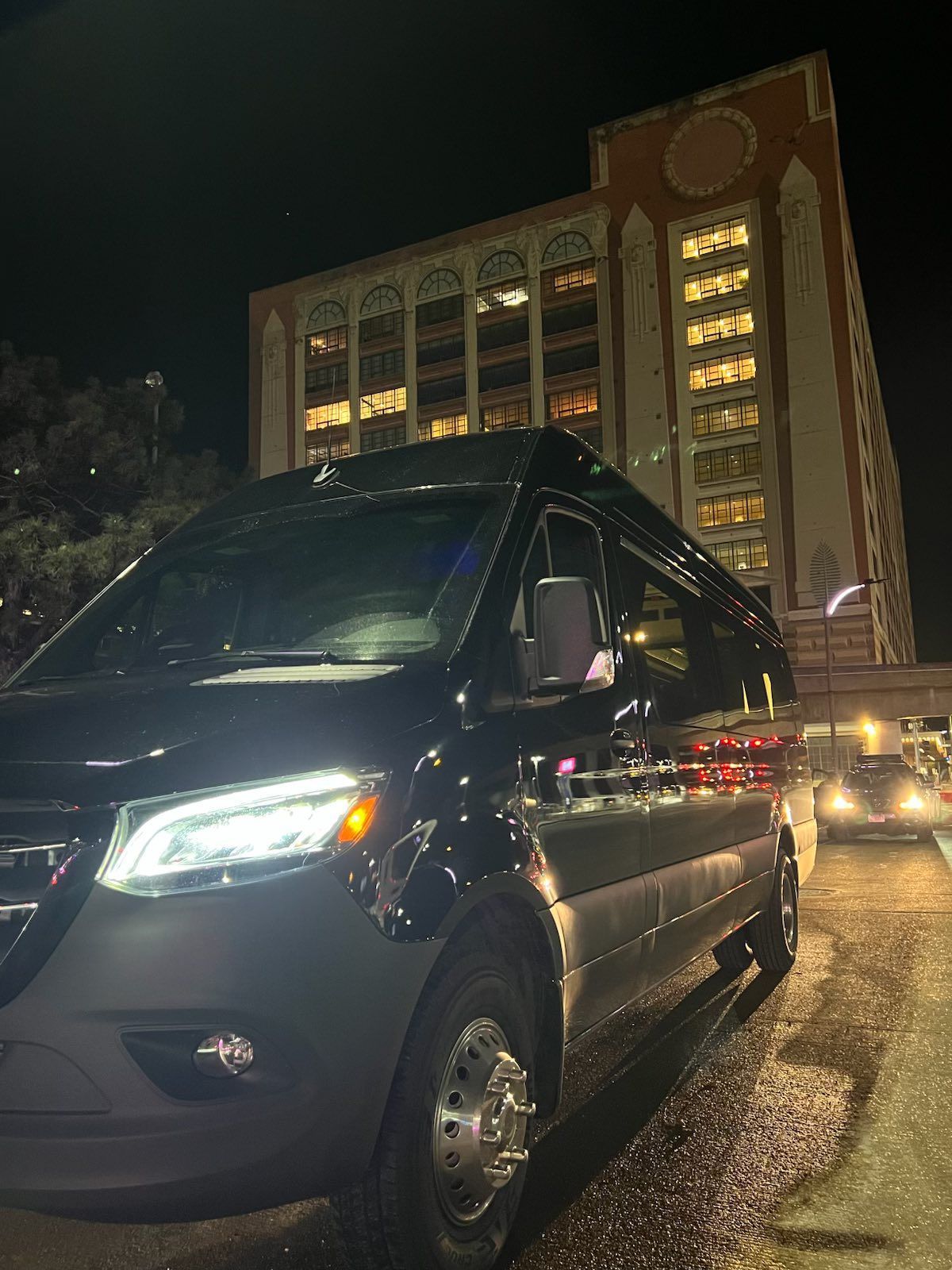 Black van parked on a wet street at night, tall brick building in the background.