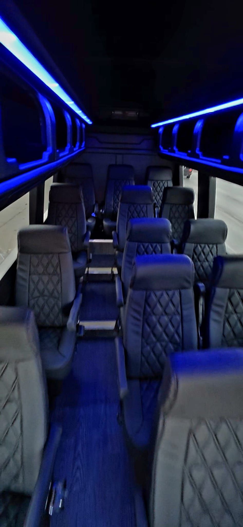 Interior view of a bus with rows of black seats and blue LED lighting.