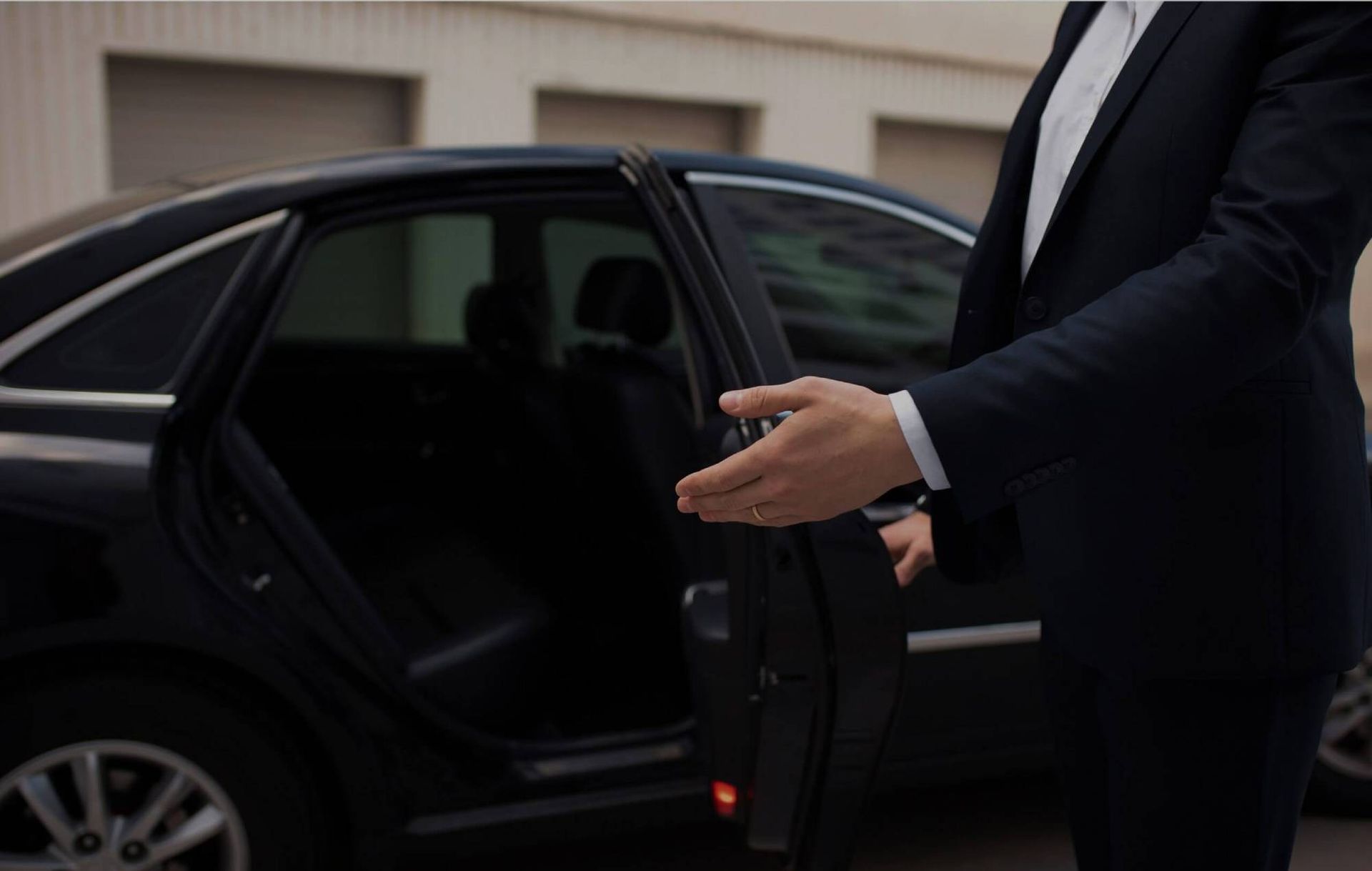 Man in suit opening a car door. Black sedan.
