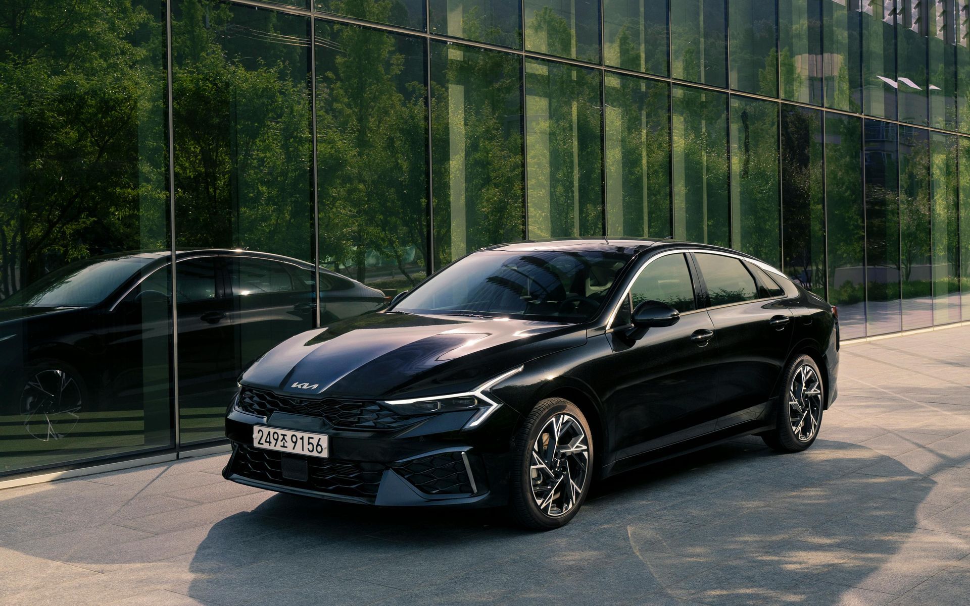 Black Kia sedan parked in front of a modern glass building.