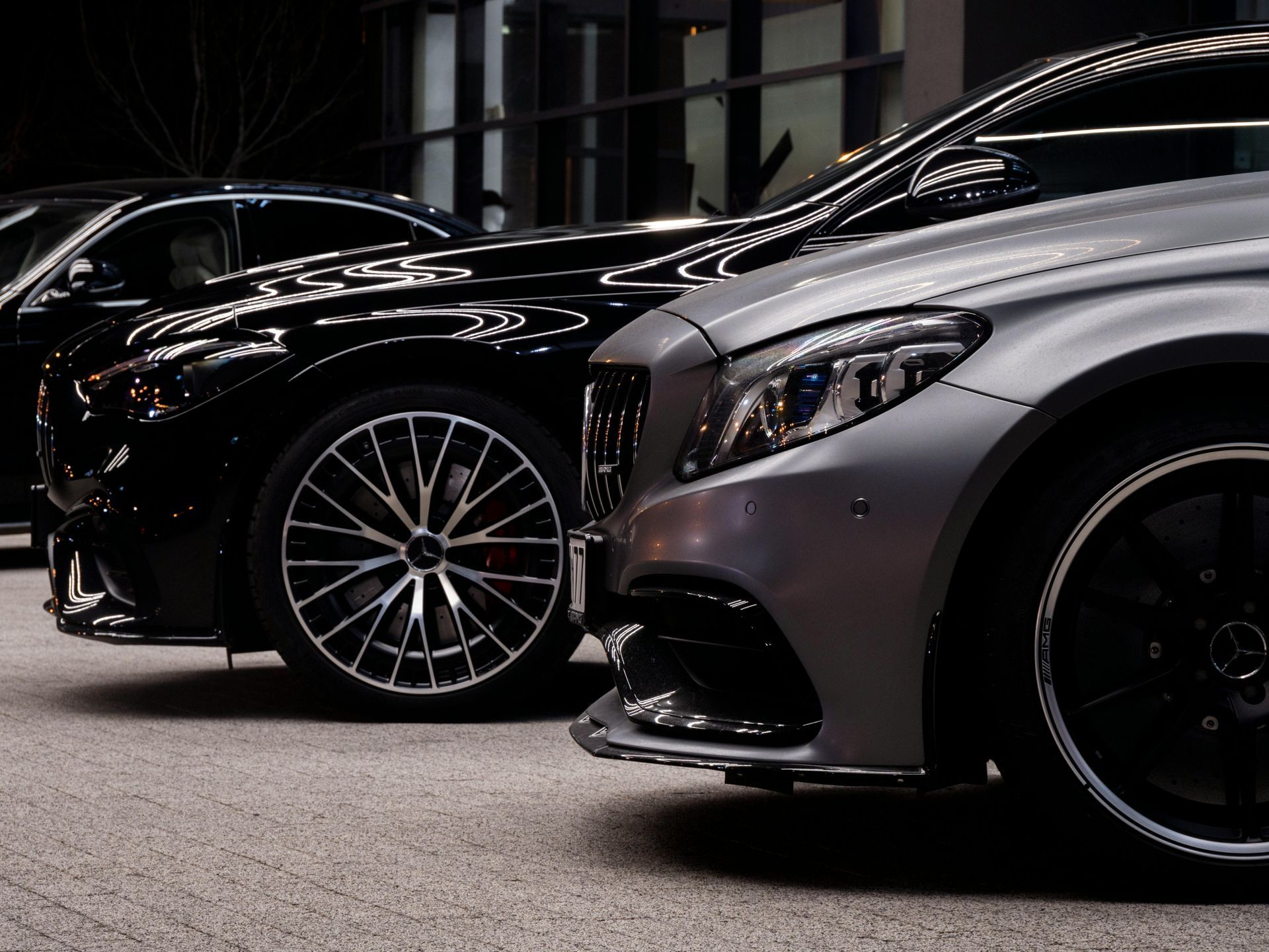 Two luxury cars, black and silver, parked indoors, wheels visible.
