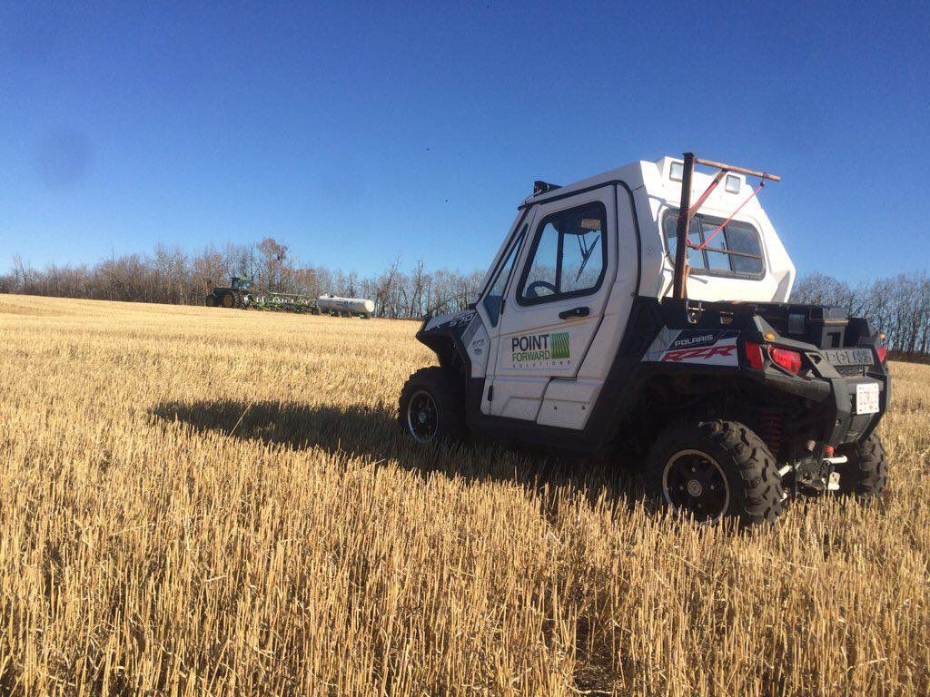 A white utility vehicle parked in a vast, harvested field under a clear blue sky.