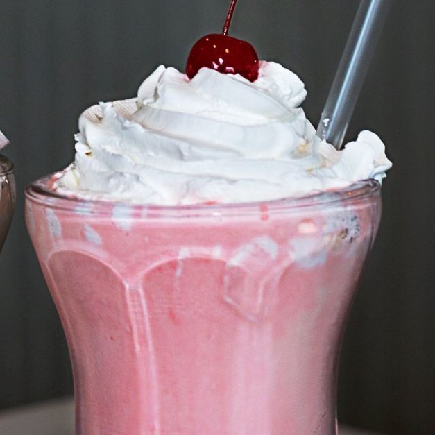 A pink milkshake with whipped cream and a cherry on top