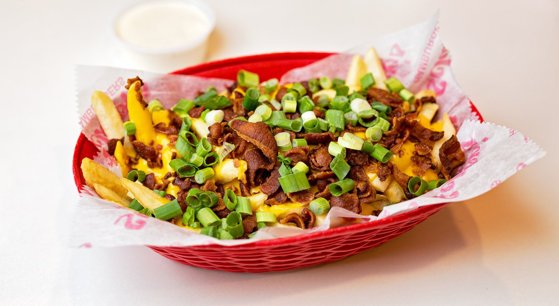 A red basket filled with french fries , cheese , bacon and green onions.