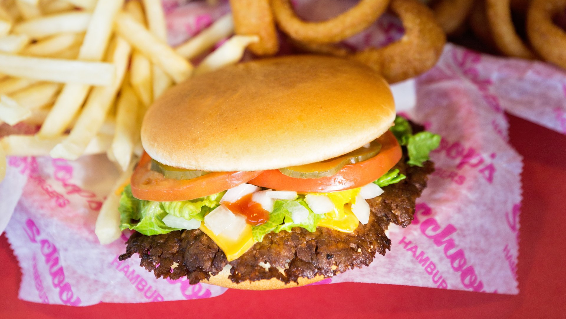 A hamburger and french fries are on a red table.