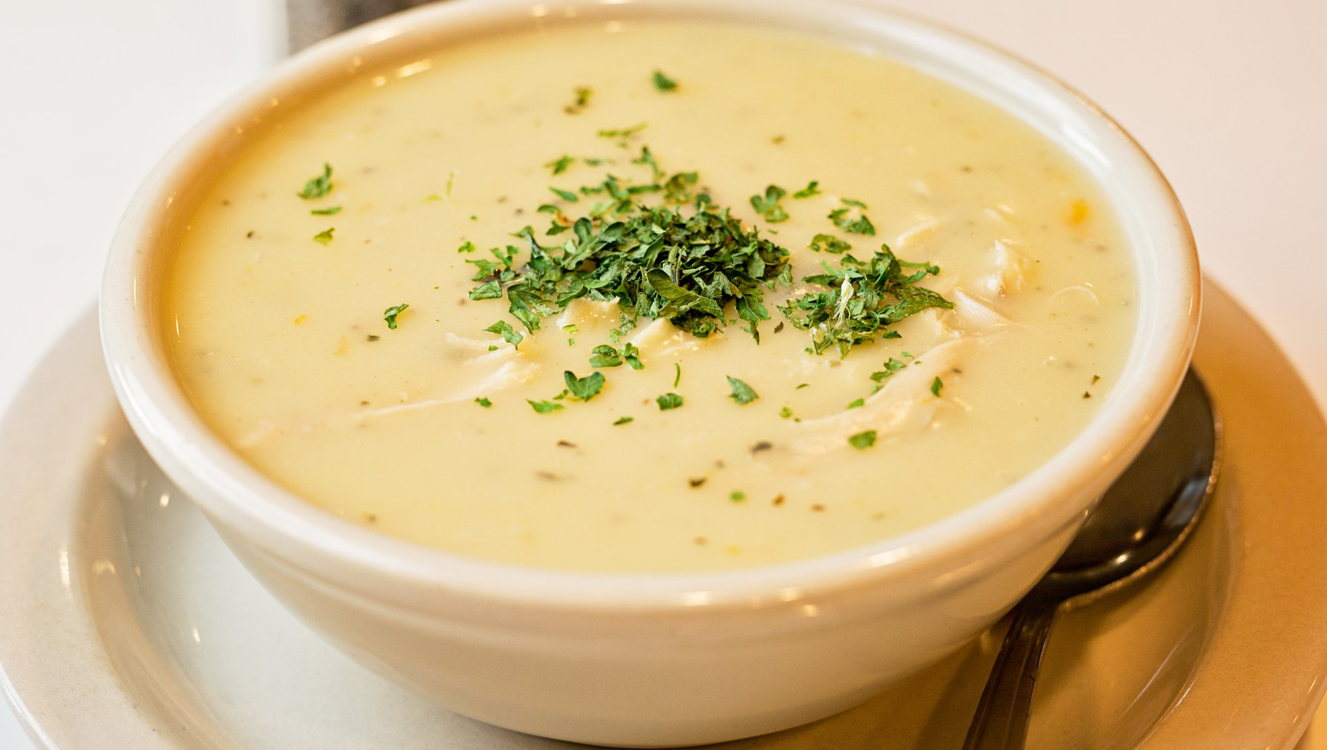 A bowl of soup with parsley on top is on a plate with a spoon.