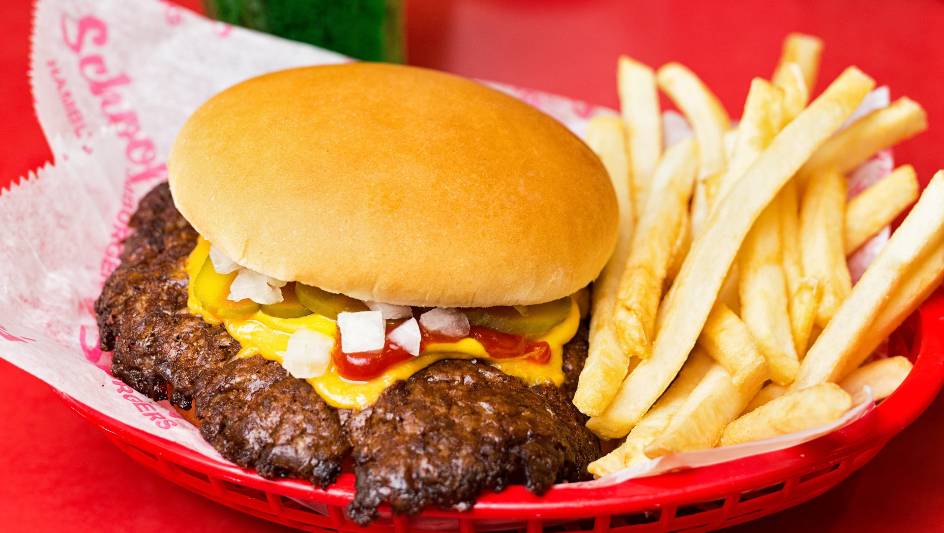 A hamburger and french fries in a red basket on a red table.