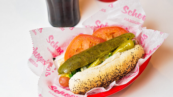 A hot dog with pickles , tomatoes and onions on a red plate.