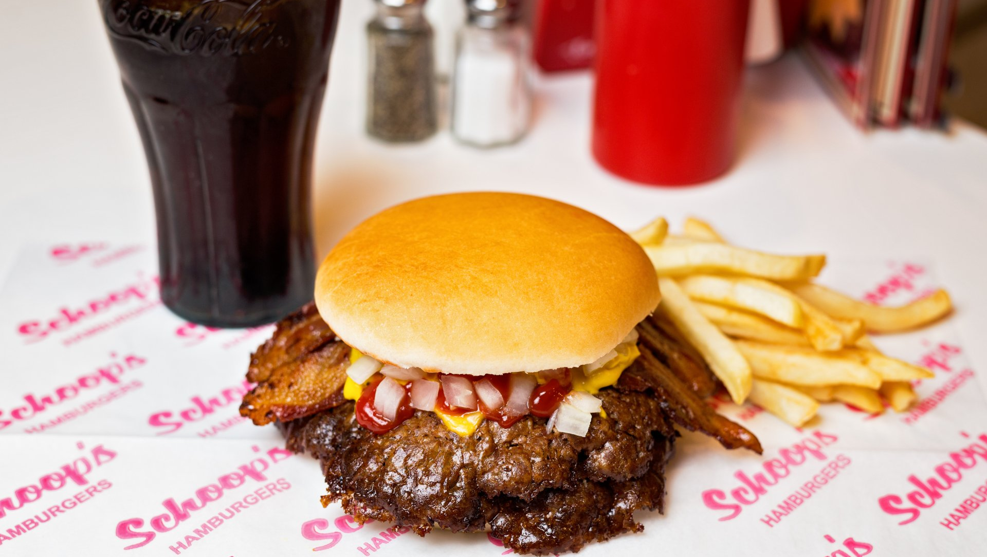 A hamburger and french fries are on a table next to a glass of soda.