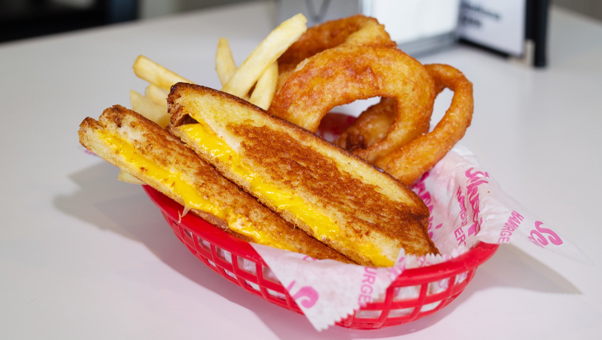 A basket of grilled cheese sandwiches and onion rings on a table.