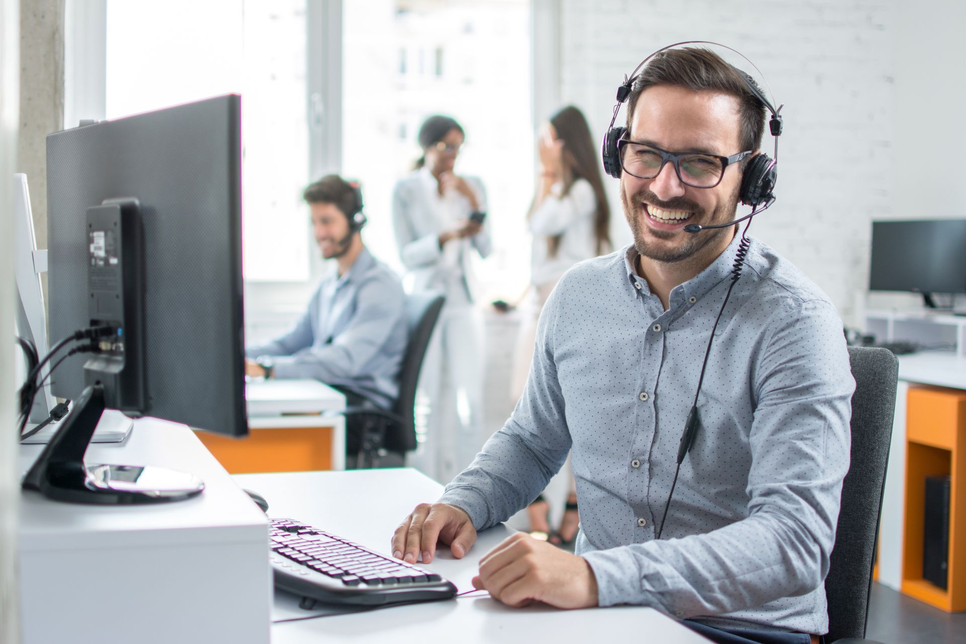 A man wearing a headset is sitting at a desk in front of a computer.