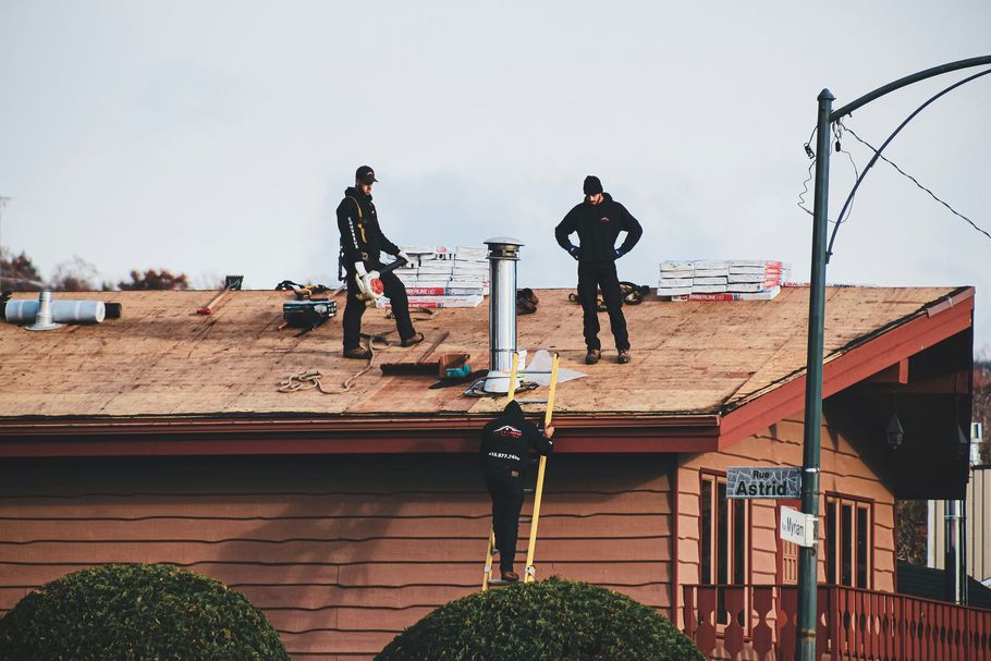 Two firefighters stand on a roof beside a chimney, inspecting or working on a building after damage.